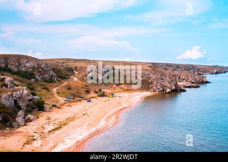 Meeresbucht mit Sandstrand und Hügeln. Touristen und Reisende ruhen sich am Ufer in einem Zeltlager aus. Stockfoto