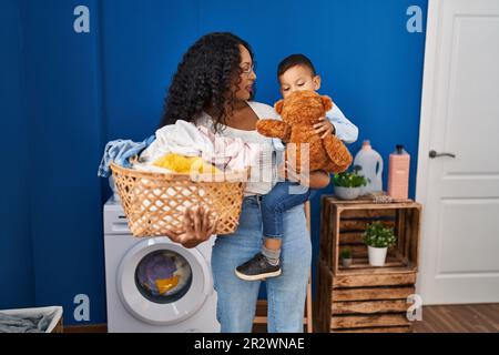 Mutter und Sohn spielen mit Teddybär und warten auf Waschmaschine in der Waschküche Stockfoto