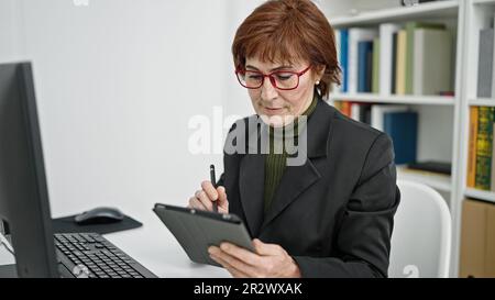 Reife hispanische Lehrerin am Computer, die sich Notizen auf dem Touchpad an der Bibliotheksuniversität macht Stockfoto