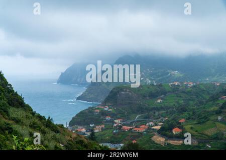 Atemberaubender Blick auf das Dorf Porto da Cruz auf Madeira, Portugal. Kleine Stadt in den Hügeln an der Küste des Atlantischen Ozeans. Dominanter Rock von Th Stockfoto