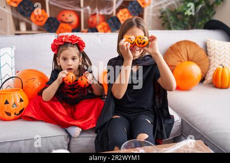 Ein süßer Junge und ein Mädchen, die halloween-Kostüme tragen und zu Hause Kürbiskörbe über die Augen halten Stockfoto
