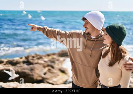 Ein Paar aus Mand und Frau umarmt sich, zeigt mit dem Finger auf das Meer Stockfoto