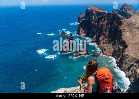 Junge Wanderer mit Rucksack, die auf einer Klippe stehen und sich auf den Hintergrund des Meeres und des Himmels freuen. eine touristische dame auf einem Berg, die die vi genießt Stockfoto