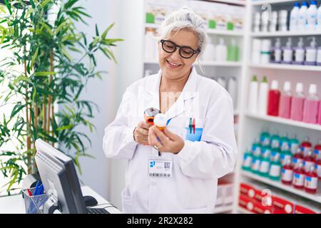 Grauhaarige Frau im mittleren Alter, Apothekerin, die in der Apotheke eine Tablettenflasche scannt Stockfoto