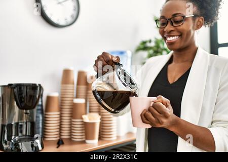 afroamerikanische Geschäftsarbeiterin, die im Büro Kaffee auf die Tasse gießt Stockfoto