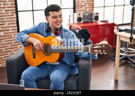 Junger nicht binärer männlicher Musiker, der klassische Gitarre im Musikstudio spielt Stockfoto