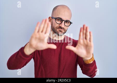 Ein junger Glatzkopf mit Bart, der auf weißem Hintergrund steht und eine Brille trägt, der mit Händen und Fingern einen Rahmen macht, Kameraperspektive Stockfoto