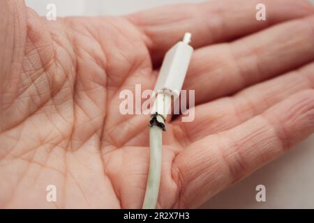 Defekter Stecker in der Hand. Gebrochenes Netzkabel in der Hand einer Frau. Defektes usb-Kabel. Smartphone-Gerät. Kabel für Mobiltelefon. Stockfoto