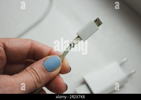 Defekter Stecker in der Hand. Gebrochenes Netzkabel in der Hand einer Frau. Defektes usb-Kabel. Smartphone-Gerät. Kabel für Mobiltelefon. Stockfoto