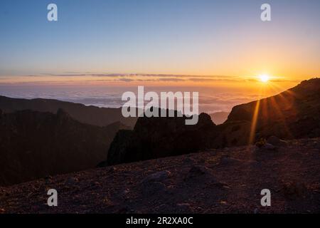 Der Sonnenaufgang in den Bergen von Madeira ist von Sonnenlicht umgeben und bietet einen malerischen Blick auf die Landschaft und den Pico Ruivo, Portugal. Stockfoto