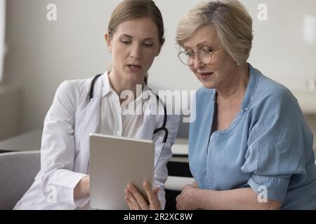 Therapeut hält Tablette, die Gesundheitstest Ergebnisse für reife Frau zeigt Stockfoto