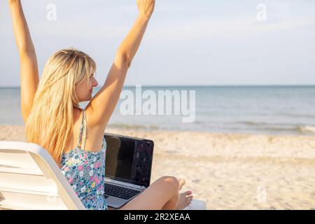 Rückansicht einer jungen blonden Frau, weibliche Freiberuflerin, die an einem Laptop arbeitet Stockfoto