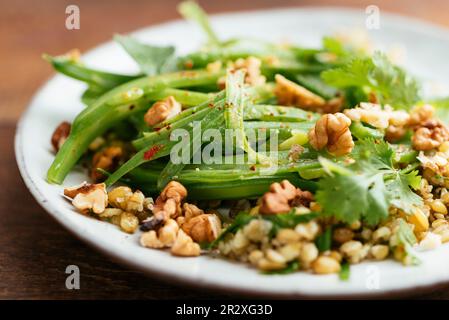 Teller mit hausgemachtem Freekeh mit grünen Bohnen und Kräutersalat. Stockfoto