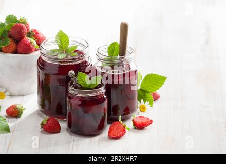 Hausgemachte Erdbeermarmelade. Marmeladengläser auf weißem rustikalem Tisch. Gesundes Frühstückskonzept. Stockfoto