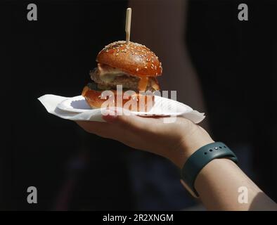 Frauen halten auf dem Farmers Street Food Markt ein Papierfach mit einem frischen Hamburger in der Hand, und sie sehen Hände, die Burger halten. Stockfoto