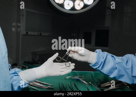 Low Angle Shot im Operationssaal, Assistentin verteilt Werkzeuge an Chirurgen während der Operation Stockfoto