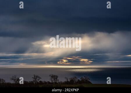 Lichtstrahlen, die durch dunkle Wolken an der Küste von Angus scheinen, Schottland Stockfoto