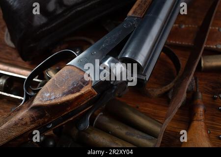 Antike 16-Gauge Break-Action glatt gebohrte Schrotflinte mit Messinggehäuse und Zubehör für Patronennachladung auf Holztisch. Stockfoto