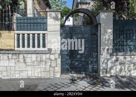 Portal eines städtischen Einfamilienhauses mit einem grau bemalten Metallzaun und einer Wand aus unregelmäßigen Steinen Stockfoto