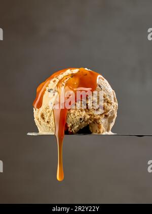Eislöffel mit fließender geschmolzener Karamellsauce auf dunkelgrauem Hintergrund Stockfoto