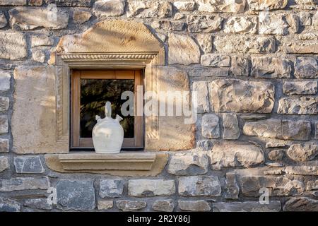 Ein weißer Botijo auf der Fensterbank eines steinernen Dorfhauses, typisch spanischer Tonkrug, um das Wasser im Sommer kühl zu halten, rustikale Atmosphäre Stockfoto