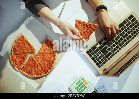 Nachhaltiger Arbeitsplatz. Blick von oben auf eine Geschäftsfrau im grünen Büro mit Pizza und Laptop. Stockfoto