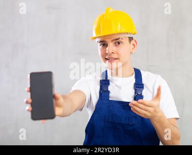 Ein lächelnder junger Mann, der in Uniform posiert und ein Handy in der Hand hat Stockfoto