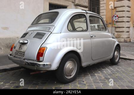 Fiat 500 in Schlacht, vernarbt, um jahrelang durch die Straßen Roms zu fahren. Trotz blasender Farbe und sichtbarer Dellen bleibt es ein Überlebender. Stockfoto