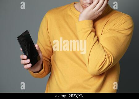 Mann hält beschädigtes Smartphone auf hellgrauem Hintergrund, Nahaufnahme. Gerät wird repariert Stockfoto