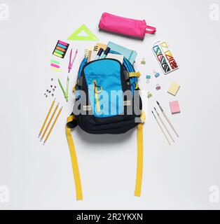 Rucksack mit verschiedenen Schreibwaren auf weißem Hintergrund, flach liegend Stockfoto