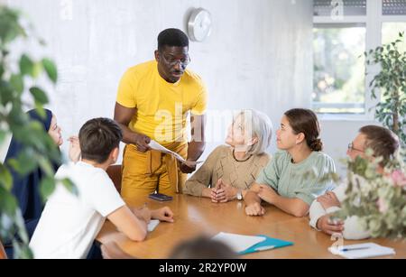 Erfahrener männlicher Trainer führt Schulungen für Menschen verschiedener Nationalitäten im Klassenzimmer durch Stockfoto