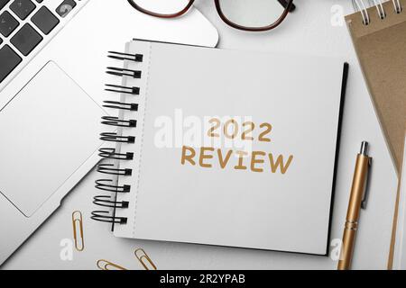 Text 2022 Bewertung geschrieben in Notizbuch, Laptop, Stift und Brille auf weißem Tisch, flach liegend Stockfoto