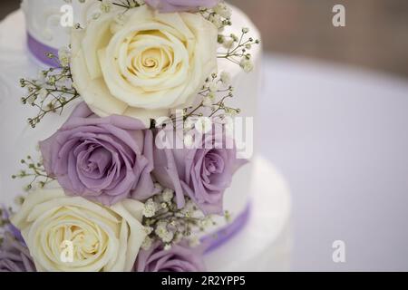 Dreistufige Hochzeitstorte mit Flieder- und cremefarbenen Rosen und lilafarbenem Band Stockfoto