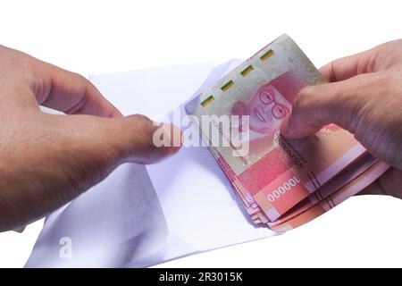 Hand nimmt Geld oder steckt es in einen Umschlag, indonesische Währung Rupien isoliert auf weißem Hintergrund Stockfoto