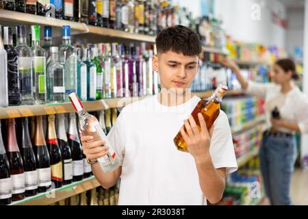 Der Mann hat im Supermarkt die Wahl zwischen Wodka und Cognac Stockfoto