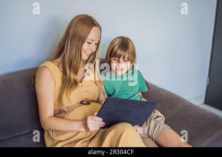 Schwangere mutter und Sohn sehen sich die Tablette an. Ein Buch lesen, einen Cartoon ansehen oder einen Videoanruf tätigen. Sehen Sie sich das Foto vom Ultraschall an Stockfoto