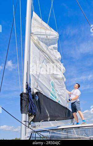 Segel setzen auf einer Yacht. Junger Mann Captan hebt das Segel einer Katamaranjacht während der Fahrt Stockfoto