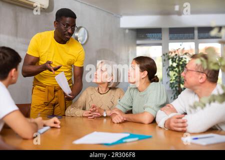 Erfahrener männlicher Trainer führt Schulungen für Menschen verschiedener Nationalitäten im Klassenzimmer durch Stockfoto