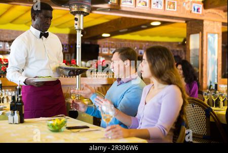 Unzufriedene Gäste, die mit dem afroamerikanischen Kellner im Restaurant in Konflikt geraten Stockfoto