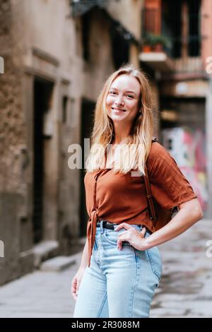 Vertikales Porträt eines jungen Kaukasiers in den Straßen der Altstadt von Barcelona. Sie posiert vor der Kamera und lächelt Stockfoto