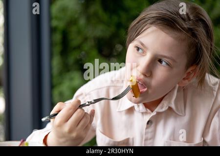 Teenager Boy hat gebratene Pommes-Kartoffeln im Sommercafé im Freien Stockfoto