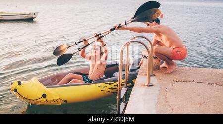 Vater mit Teenager Sohn Vorbereitung Abendfahrt Laden Ruder in einem aufblasbaren Kajak. Adriaküste Hafen in Kroatien in der Nähe von Sibenik Stadt. Urlaub A Stockfoto