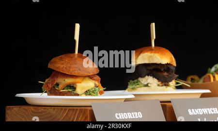 Chorizo-Burger im Vordergrund mit Sandwich mit Rinderbacke im Hintergrund beim Street Food Festival in Prag, dunkler Hintergrund, keine Menschen, Closeu Stockfoto