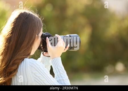 Rückansicht Porträt eines Fotografen, der Fotos mit einer spiegellosen Kamera in einem Park macht Stockfoto