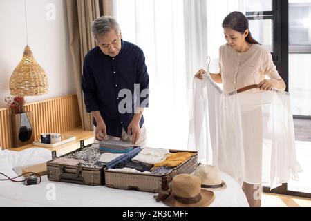 Glückliches reifes chinesisches Paar, das Koffer für den Urlaub packt Stockfoto