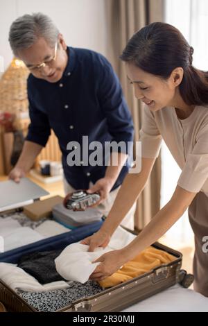 Glückliches reifes chinesisches Paar, das Koffer für den Urlaub packt Stockfoto