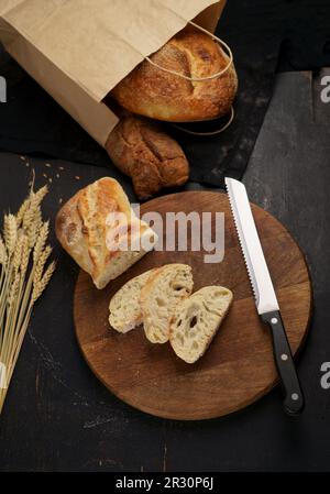 Nahaufnahme von frischem Brot auf dem Tisch. Frisches Brot auf dem Küchentisch Vollkornbrot auf Küchenholzteller mit einem Messer zum Schneiden. Frisch gebackener Roggen br Stockfoto