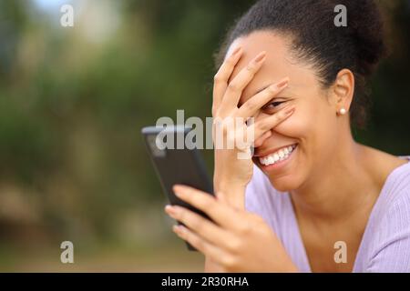 Peinliche schwarze Frau, die ein Smartphone benutzt und dich ansieht Stockfoto