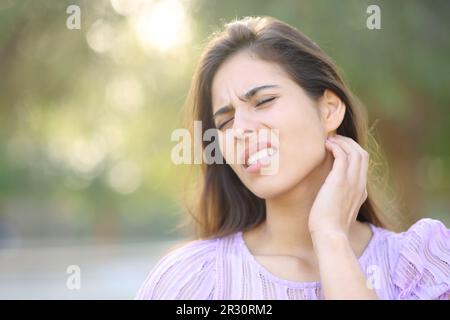 Gestresste Frau, die sich nach Insektenstich im Park am Hals kratzt Stockfoto