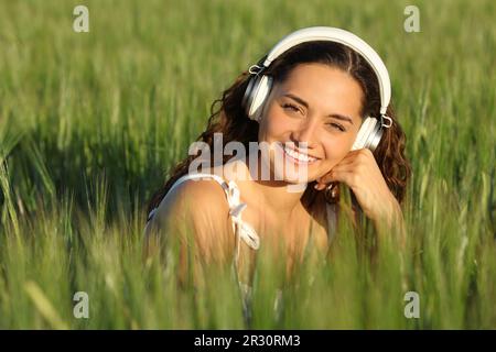 Eine glückliche Frau auf einem grünen Feld sieht dich mit Heaphon an Stockfoto